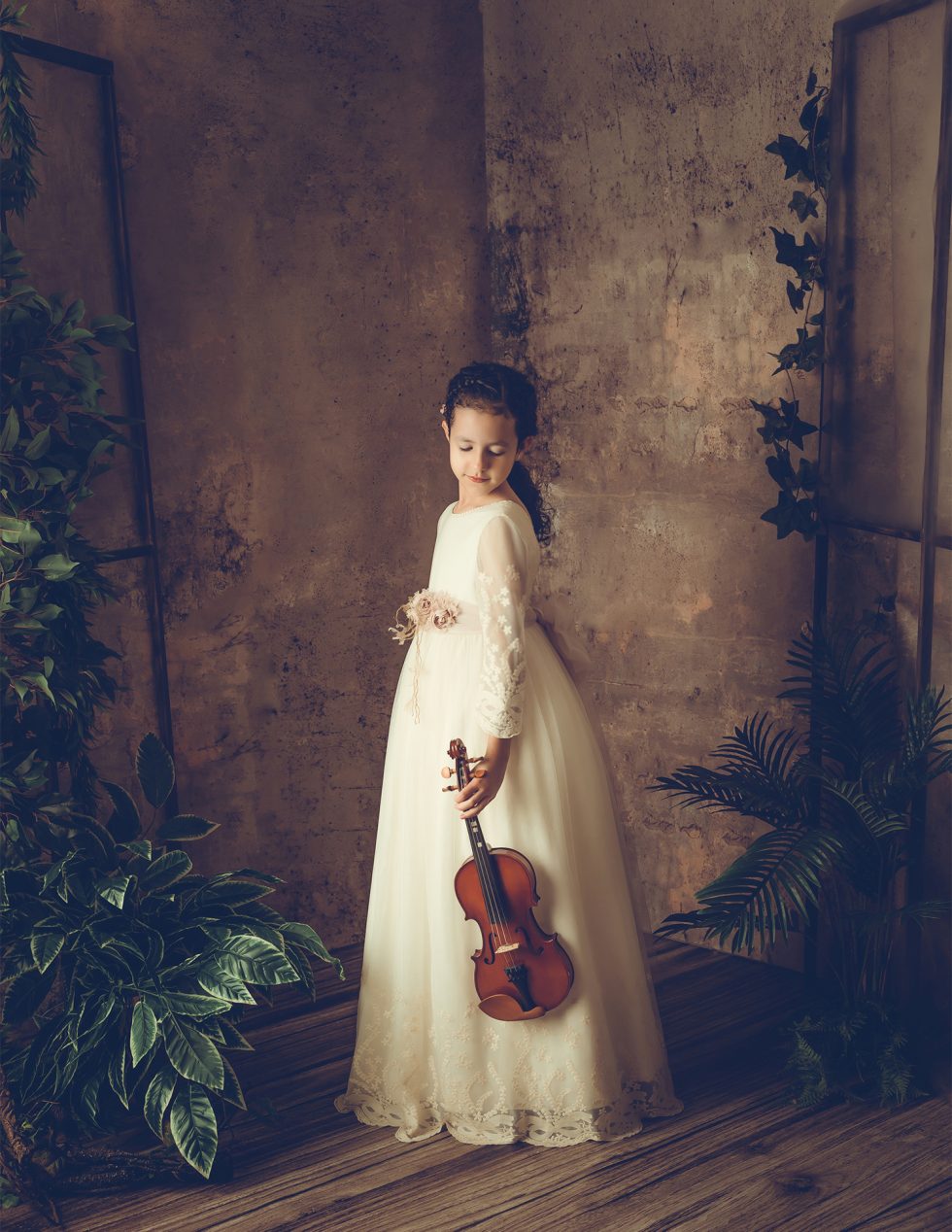 Niña tocando el violín para su sesión de fotos de primera comunión y álbum con el reportaje en estudio de fotografía en Madrid