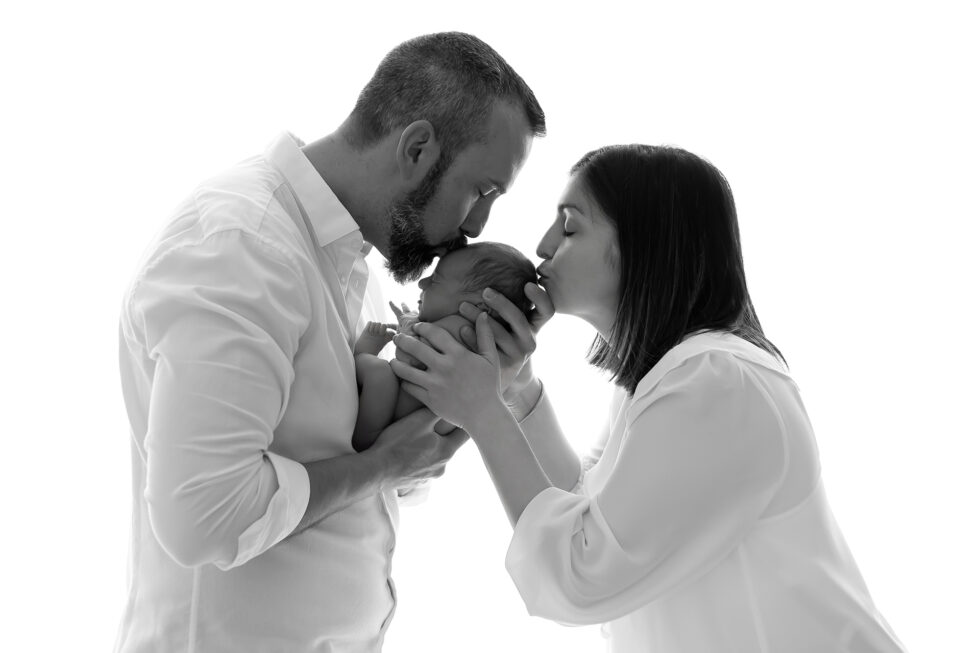 Padres besando a su bebé recién nacido en una sesión de fotos recién nacido en blanco y negro, realizada en estudio en Getafe, Madrid