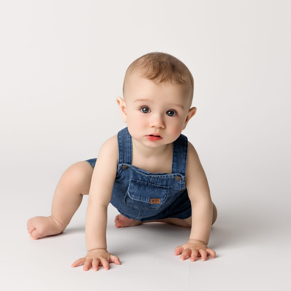 bebé gateando con peto vaquero durante una sesión de fotografía infantil en estudio