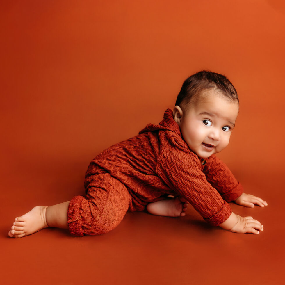bebé gateando en estudio durante una sesión de fotos de bebé con fondo naranja