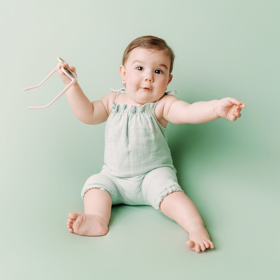 bebé sentado con gafas durante una sesión de fotos de bebé en estudio con fondo verde