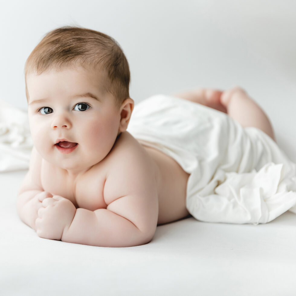 bebé tumbado sobre sábana blanca durante una sesión de fotografía infantil en estudio en Madrid