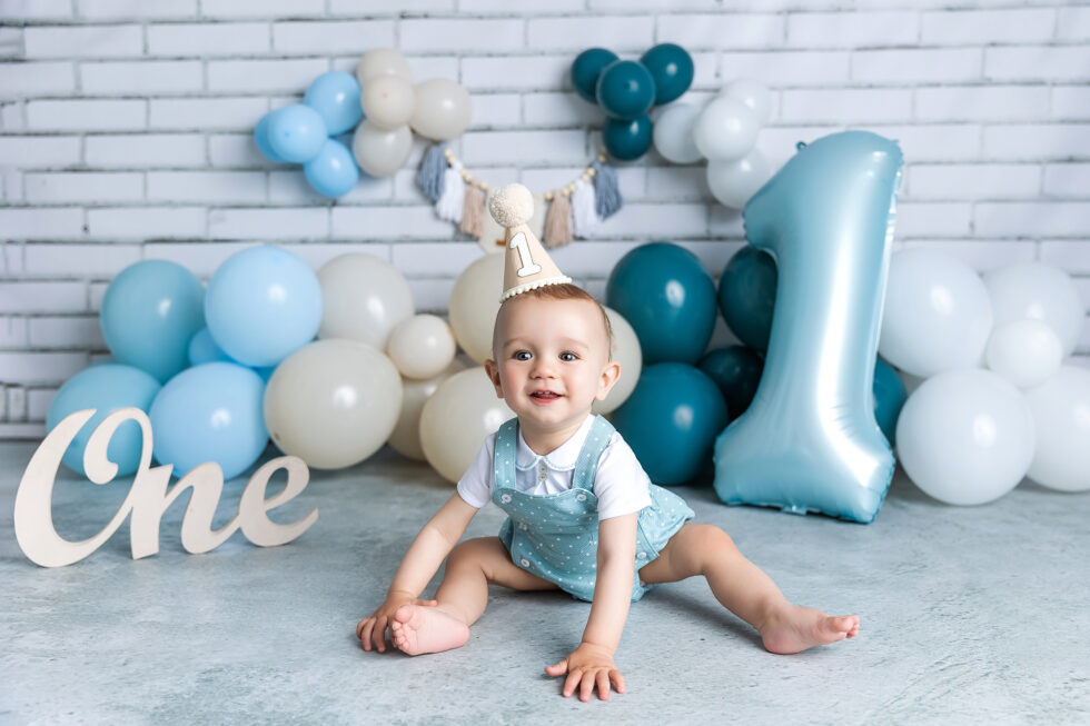 bebé celebrando su primer cumpleaños durante una sesión de fotos infantil con globos y número uno en estudio en Getafe Madrid