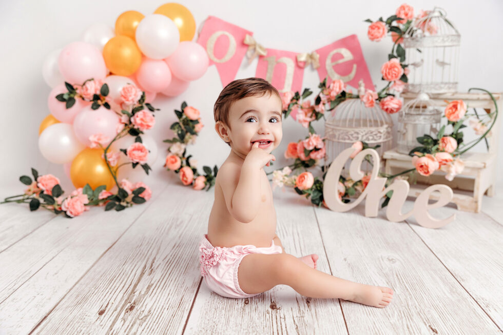 bebé celebrando su primer cumpleaños con decoración floral durante una sesión de fotos infantil en estudio